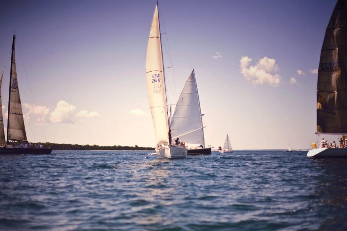 Five sailboats on the blue water of Lake Huron with light blue sky and clouds overhead.