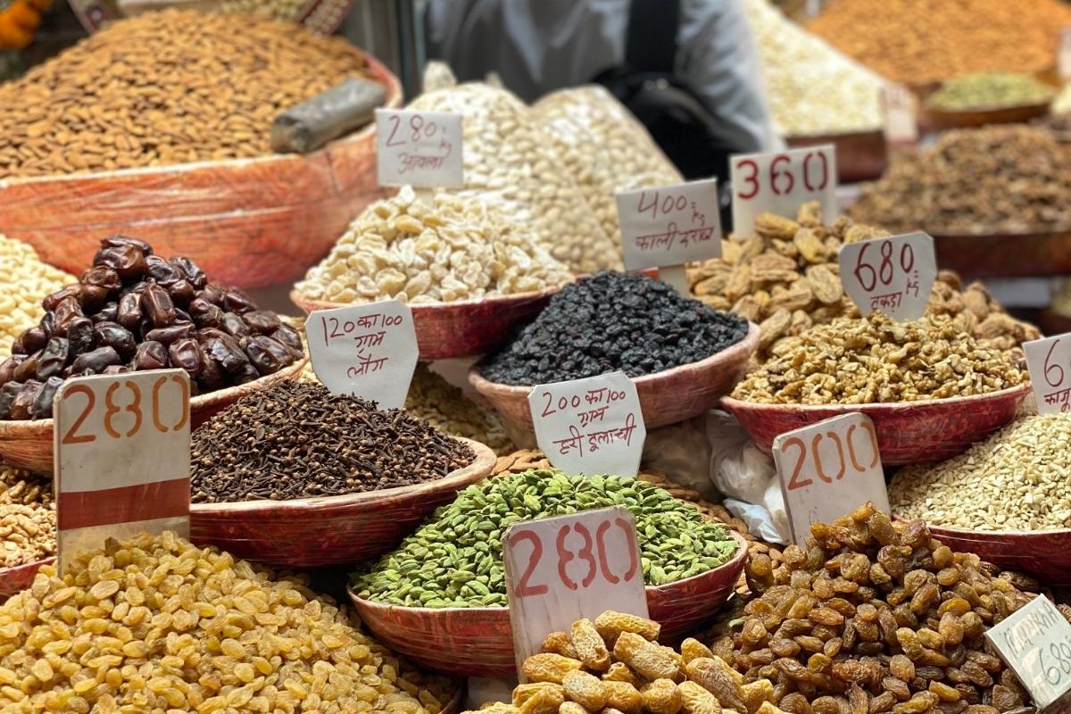 Close up photo of various green, brown, and dark spices in bowls with price tags in a Delhi Spice Market