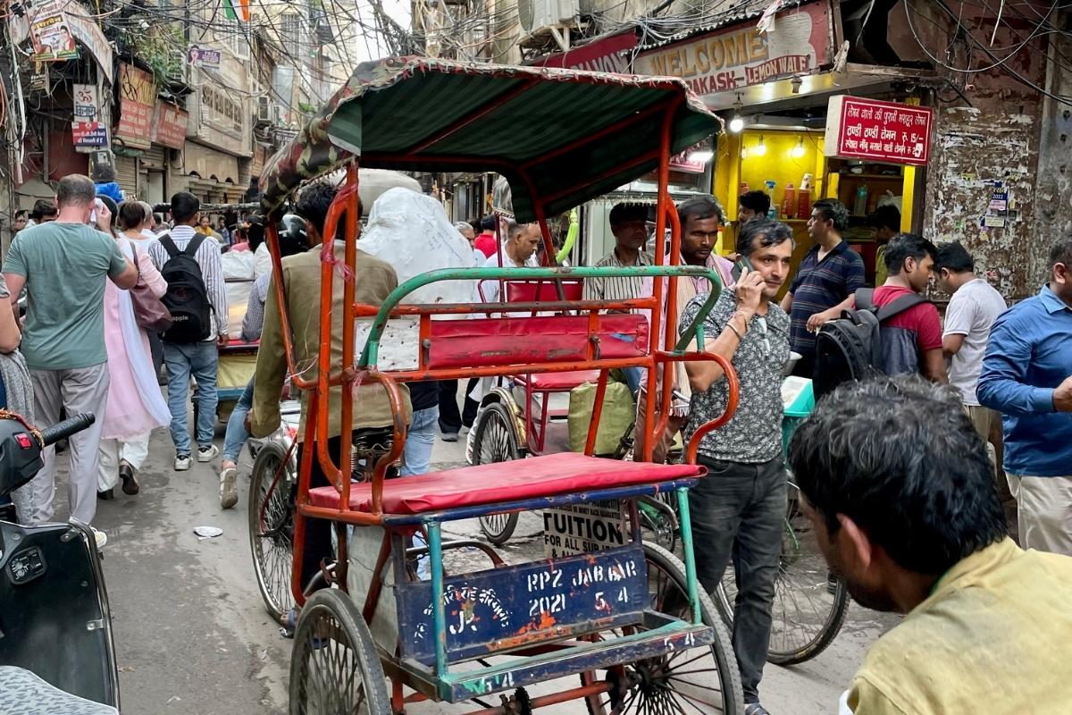 Narrow Old Town Delhi street, crowded with pedestrians, shops, and rickshaws