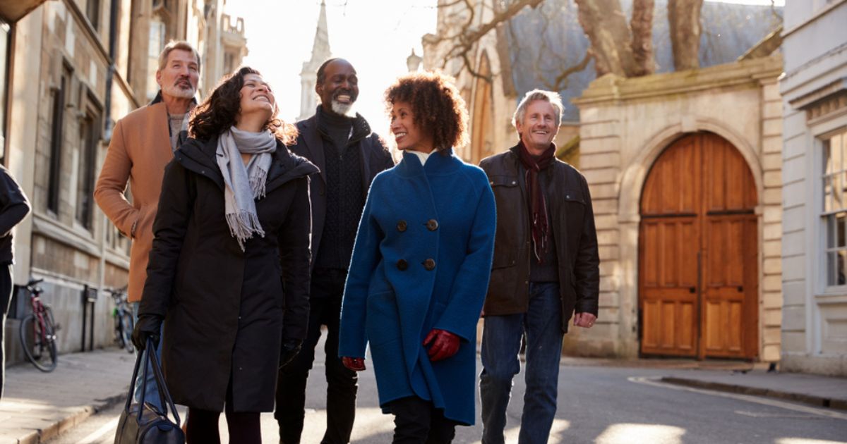 A group of mature friends walking and smiling down a European street in fall